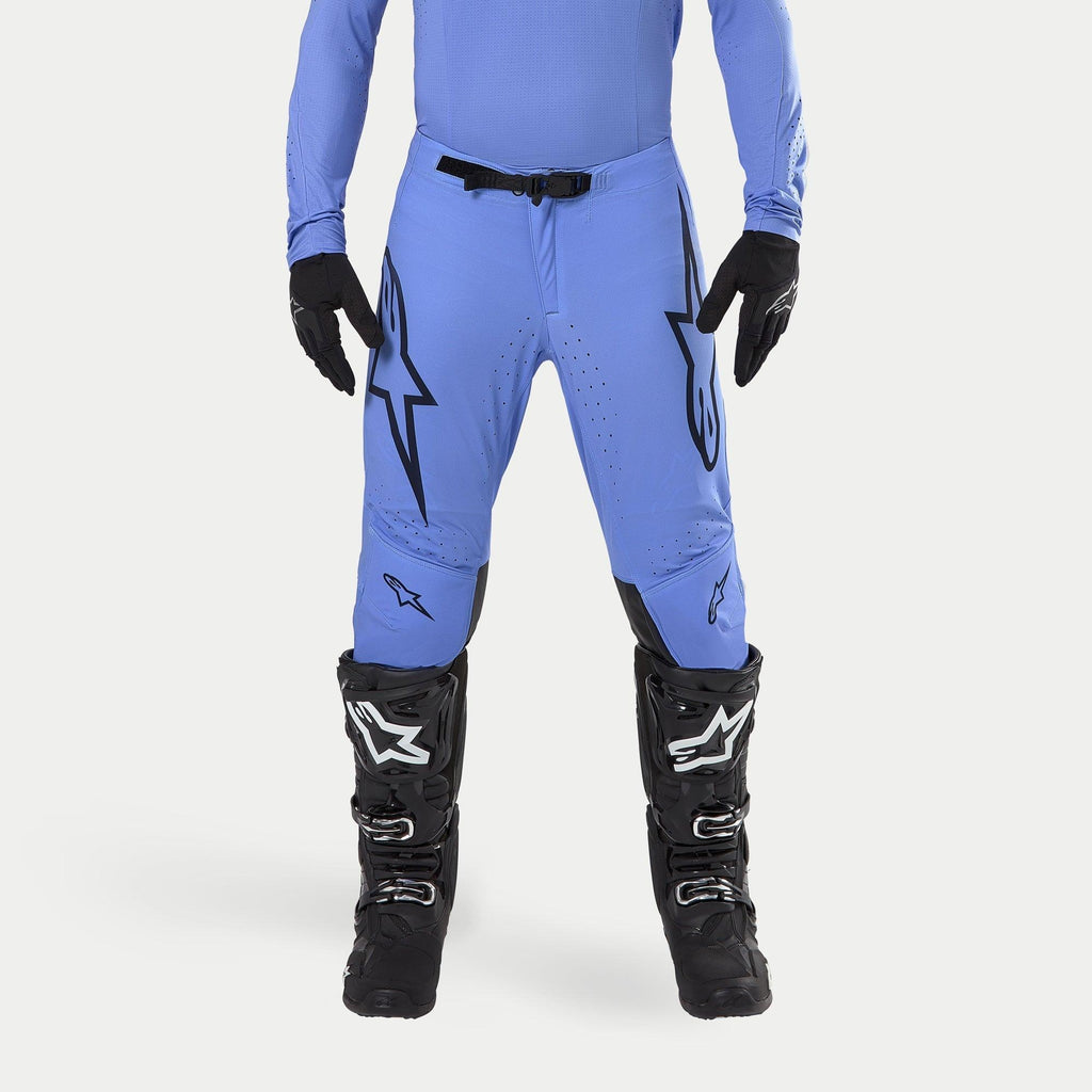 Alpinestars 2024 Supertech Dade Pants, calças de motocross, azul claro, com grandes logótipos Astars pretos nas coxas, fivela de cintura preta, usadas com botas de motocross pretas e camisola azul a condizer, vestuário profissional de corrida todo-o-terreno
