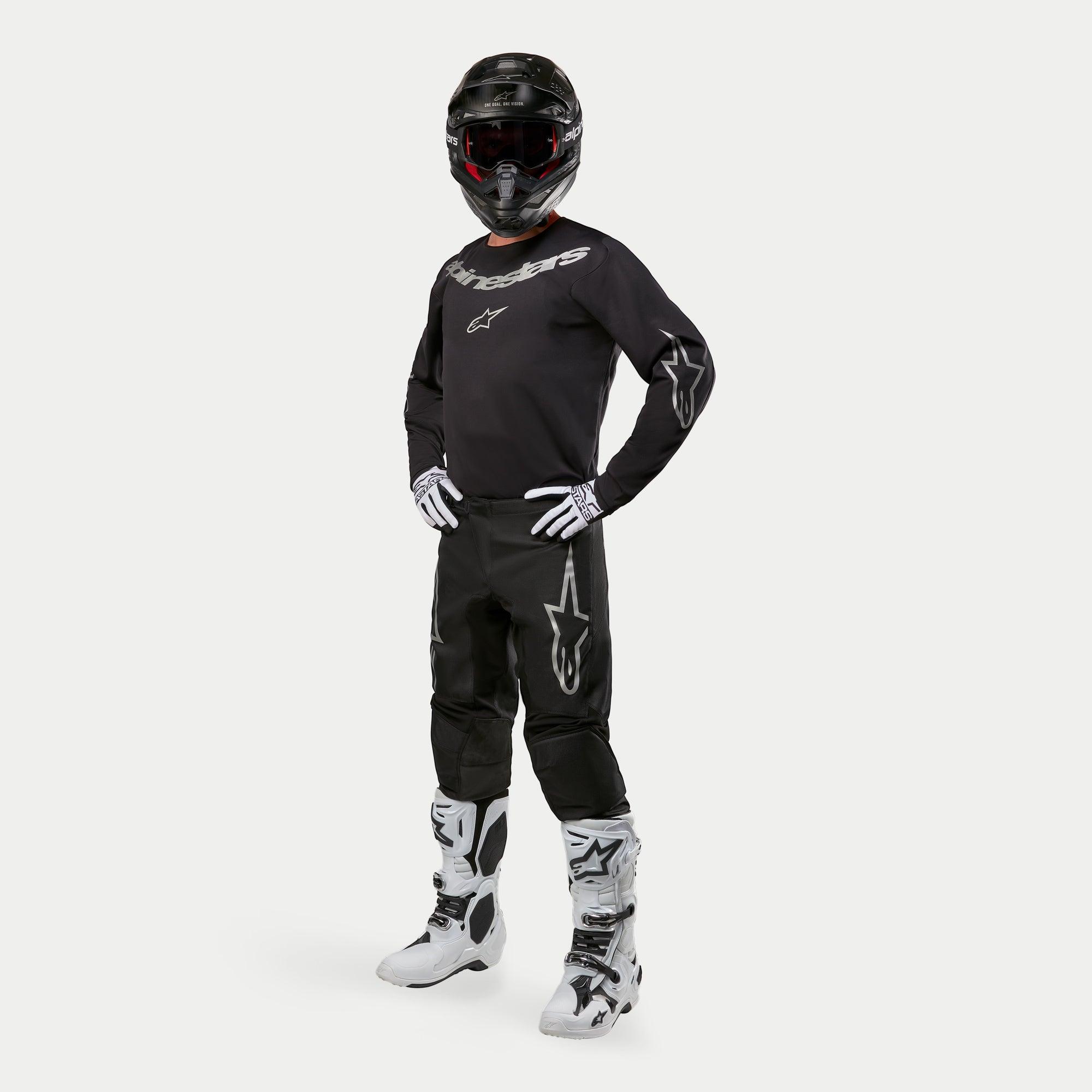 Alpinestars 2024 Fluid Graphite Pants, Motocross Pants, Black and Silver, worn with matching black jersey, black helmet, white gloves, and white boots, featuring silver Alpinestars logos on the thighs, ergonomic athletic fit for off-road racing.