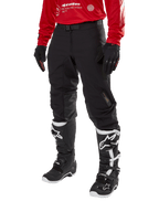 Alpinestars Techdura Pants, Black off-road motorcycle pants, worn with a red long-sleeve jersey and black and white motocross boots, featuring rugged stretch polyamide construction, leather inner knee reinforcements, and an adjustable buckled belt for enduro riding.