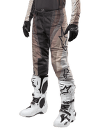 Alpinestars 2024 Techstar Pneuma Pants, calças de motocross, bege escuro e cinzento, usadas com botas brancas e pretas e luvas pretas, com um padrão ondulado e um logótipo de estrela grande, equipamento durável para corridas todo-o-terreno