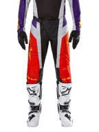 Alpinestars 2024 Techstar Ocuri Pants, calças de motocross, em laranja vibrante, roxo e preto, usadas com camisola a condizer, luvas pretas e botas brancas, com painéis frontais em laranja, detalhes roxos na cintura e secções cinzentas perfuradas, design técnico para corridas todo-o-terreno