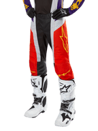 Alpinestars 2024 Techstar Ocuri Pants, calças de motocross, laranja vibrante, preto e branco com gráfico de estrela amarela, usadas com camisola roxa e botas brancas, equipamento de alta performance para competição todo-o-terreno