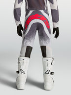 Alpinestars Supertech Swan, calças de motocross para juventude, cinzentas e vermelhas fluo, vista traseira, ajuste atlético premium com reforço no assento