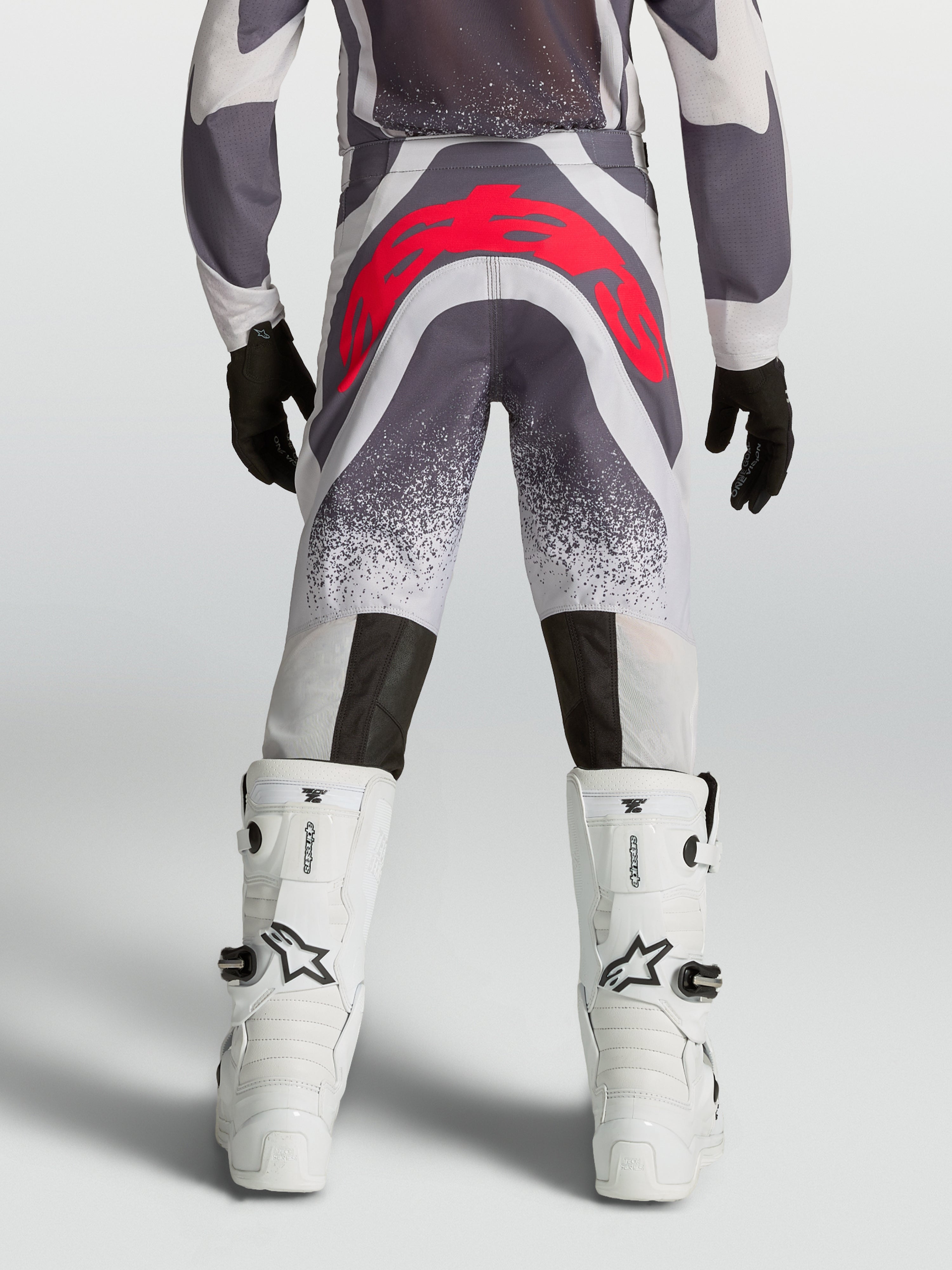 Alpinestars Supertech Swan, calças de motocross para juventude, cinzentas e vermelhas fluo, vista traseira, ajuste atlético premium com reforço no assento