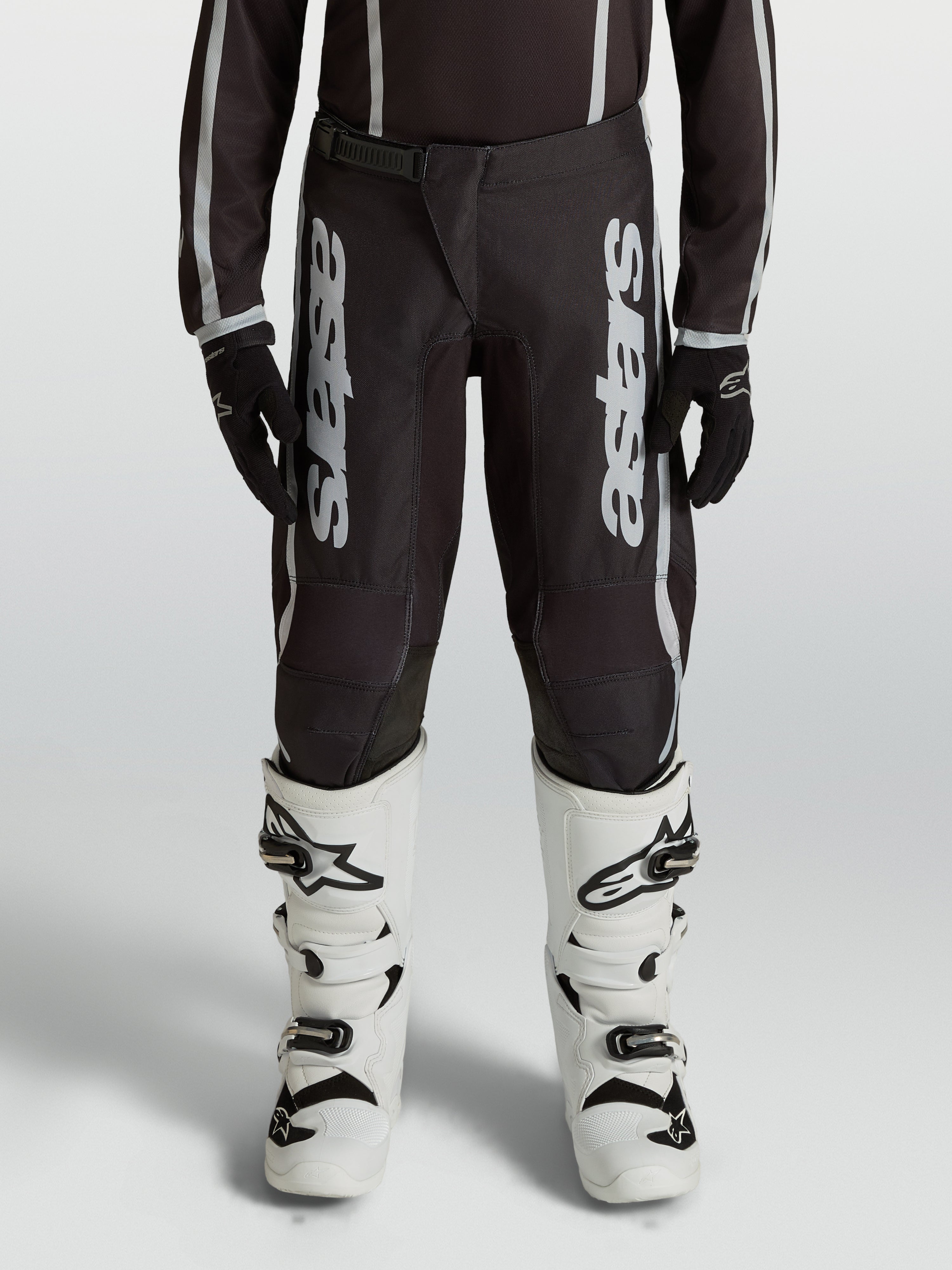 Alpinestars Fluid Apex V2, calças de motocross para juventude, pretas e prateadas, em polifabric 600D com pernas pré-curvadas.