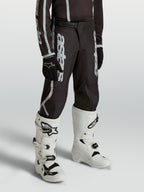 Calças Alpinestars Fluid Apex V2 Juventude para jovens pilotos, pretas e prateadas, com ajuste ergonómico pré-curvado.