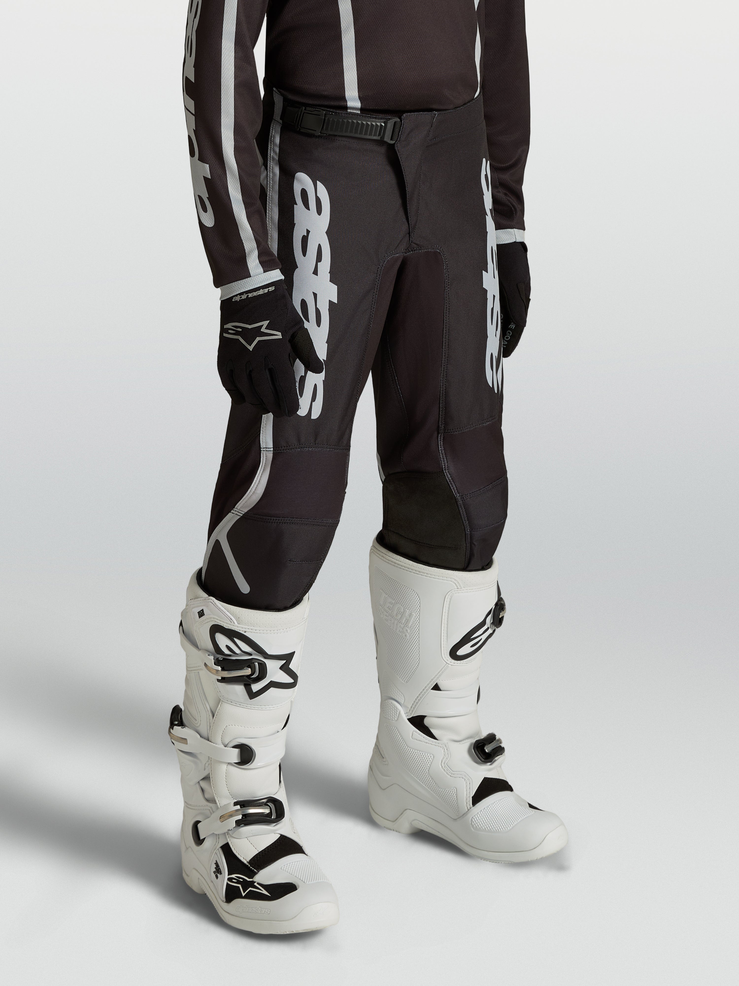 Calças Alpinestars Fluid Apex V2 Juventude para jovens pilotos, pretas e prateadas, com ajuste ergonómico pré-curvado.