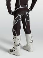 Alpinestars Calças Fluid Apex V2 Juventude, calças de motocross, pretas e prateadas, vista traseira com botas brancas.