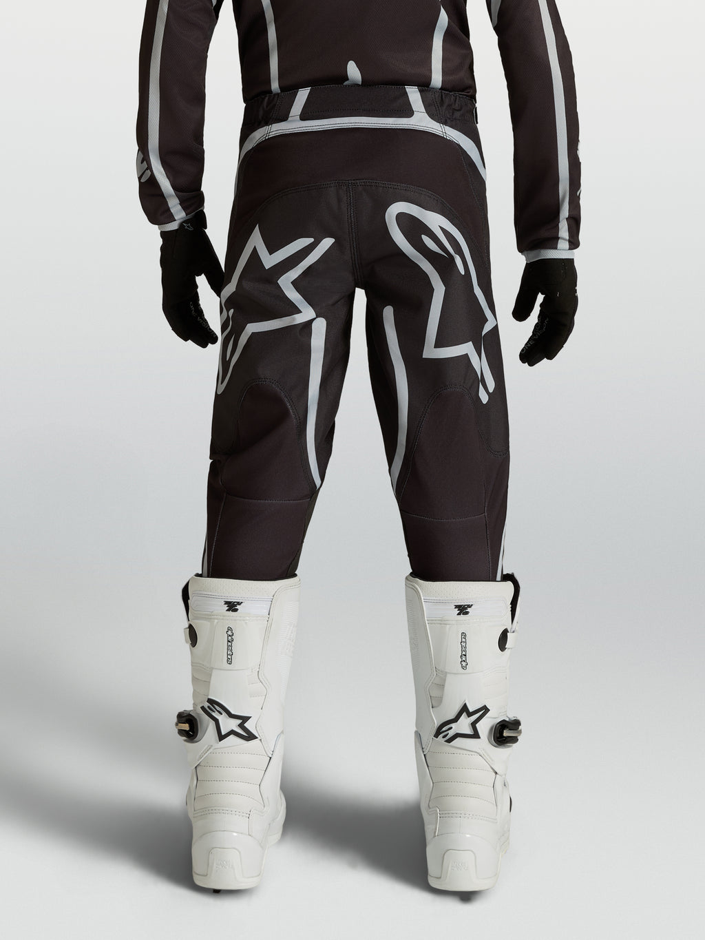 Alpinestars Calças Fluid Apex V2 Juventude, calças de motocross pretas e prateadas, vista traseira com logótipos de estrela.