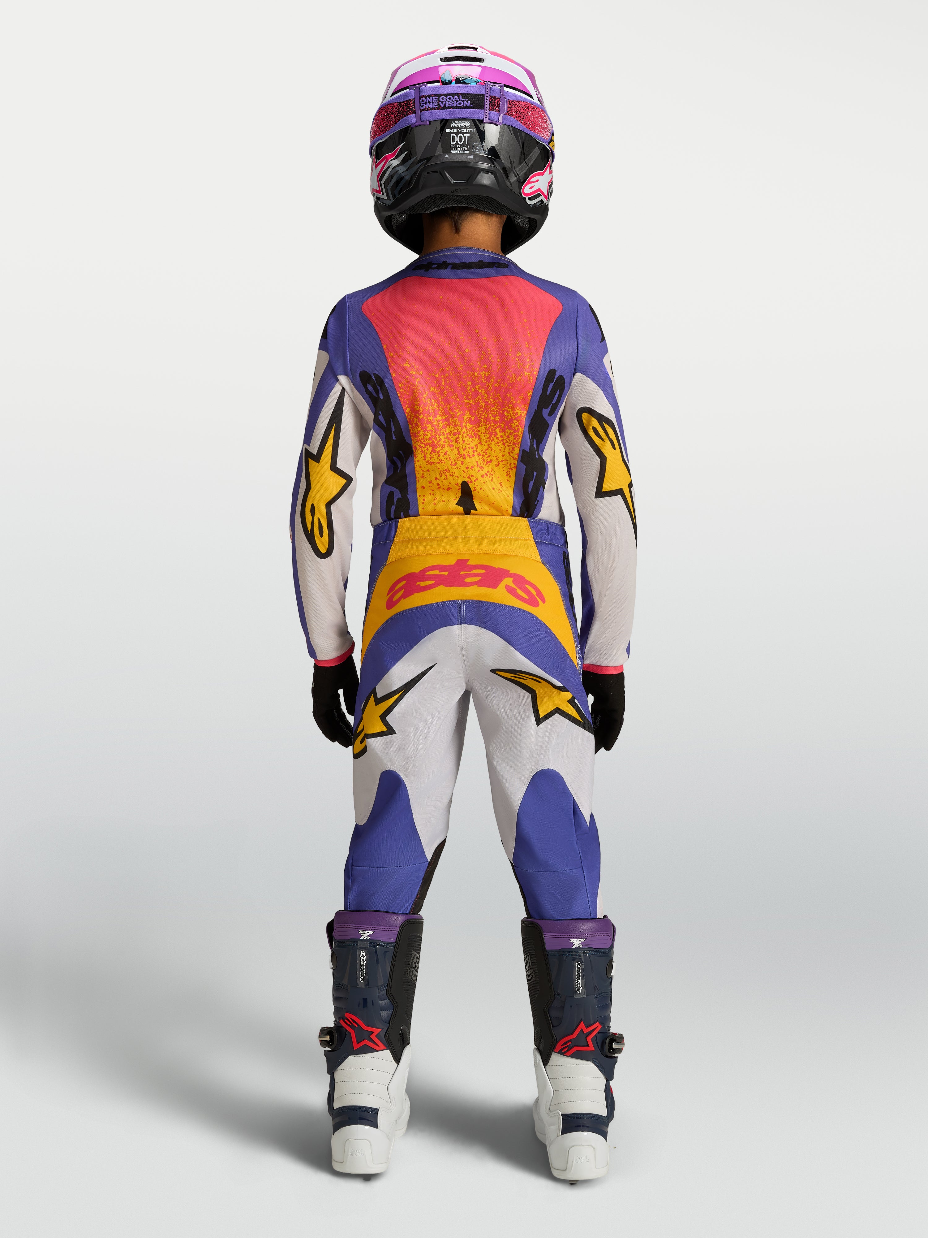 Alpinestars Calças Fluid Drag Juventude 2027, calças de motocross para jovens, azuis, brancas e amarelas, vista traseira de piloto em performance off-road.