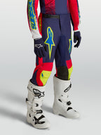 Alpinestars Calças Fluid Drag Juventude, equipamento de motocross azul-marinho e vermelho com detalhes néon e botas brancas de performance.