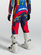 Alpinestars Calças Fluid Drag Juventude, calças de motocross azul-marinho e vermelho, vista traseira com botas brancas.