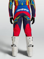 Calças Alpinestars Fluid Drag Juventude, motocross, azuis e vermelhas, em tecido 600D com corte ergonómico traseiro.