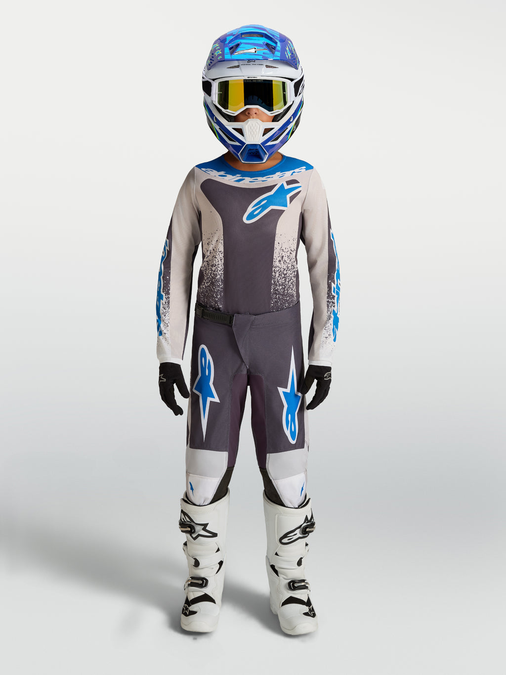 Alpinestars Calças Fluid Drag Juventude, calças de motocross todo-o-terreno cinzentas e azuis, no modelo com botas brancas.