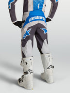Alpinestars Calças Fluid Drag Juventude, calças de motocross cinzentas e azuis, vista traseira num piloto com botas brancas.