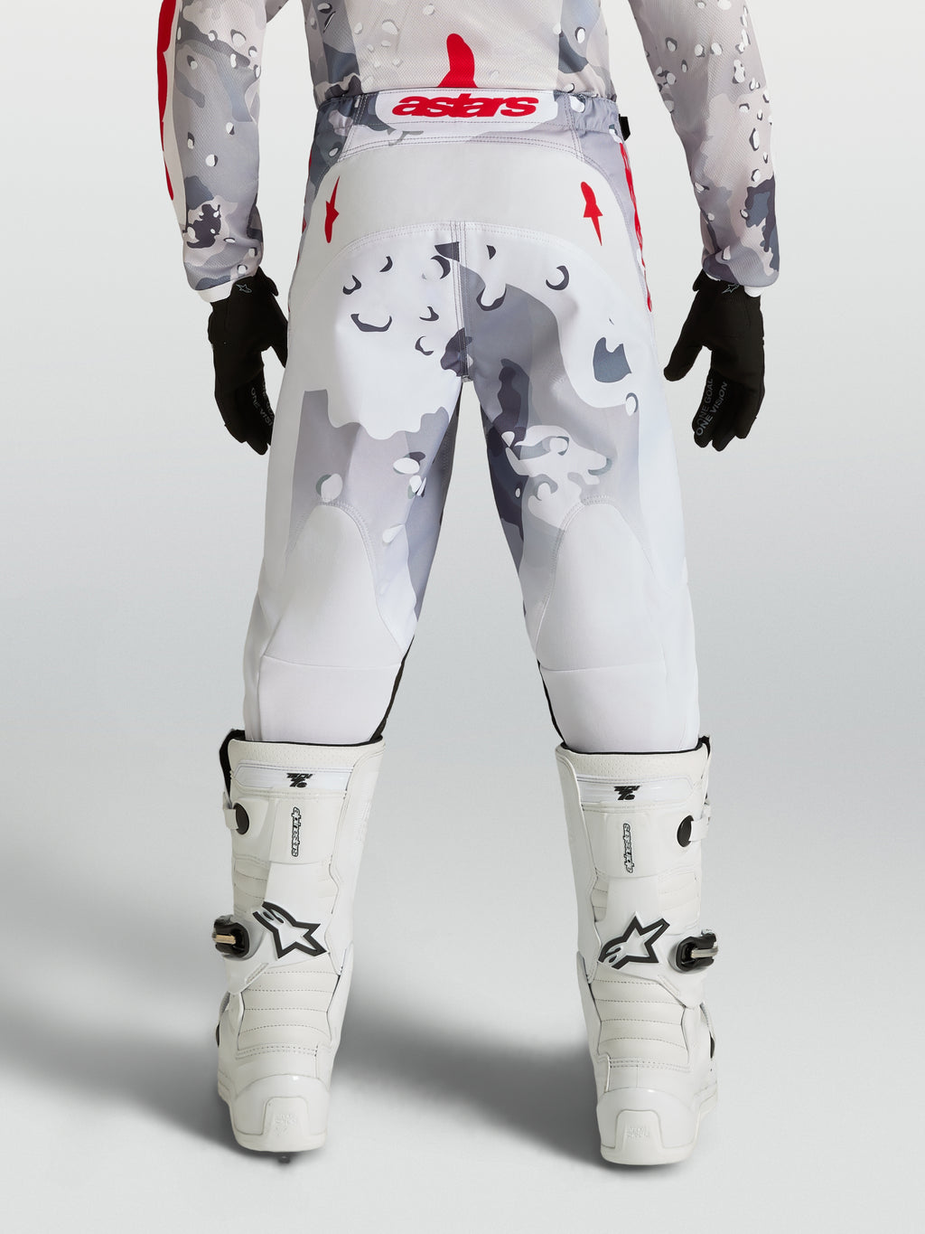 Alpinestars calças Fluid Lone Juventude, calças de motocross em cinzento camuflado e branco com detalhes em vermelho, vista traseira no piloto.