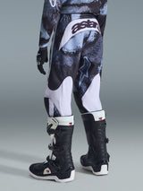 Calças Alpinestars 2026 Youth Fluid Lahnd, calças de motocross, Iron Camo com detalhes brancos, vista traseira mostrando a marca 'astars' no assento, usadas com camisola camuflada a condizer e botas de motocross Tech 3 pretas e brancas.