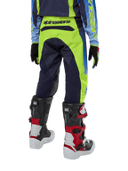Alpinestars Youth 2024 Racer Hoen Pants, calças de motocross, amarelo néon e azul marinho, vista traseira mostrando a marca Alpinestars em destaque no cós, usadas com botas Tech Series pretas e vermelhas e camisola a condizer, ajuste desportivo durável para jovens pilotos de todo-o-terreno