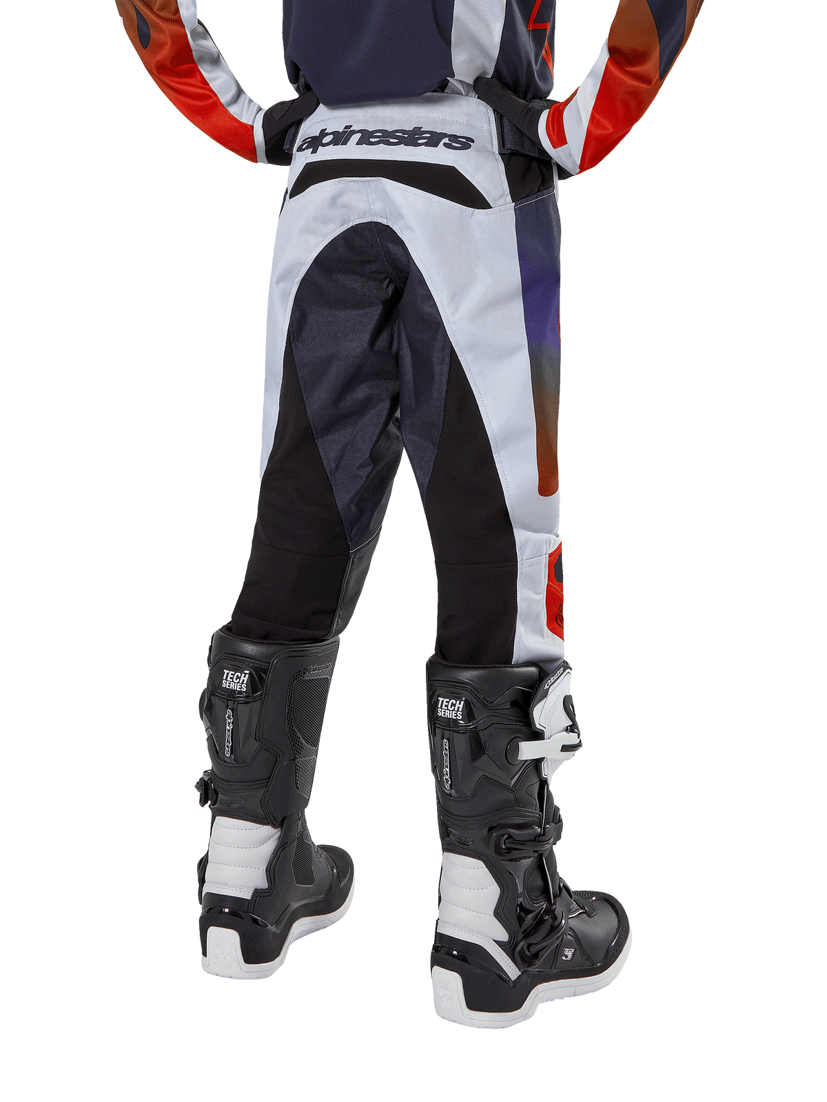 Alpinestars Youth 2024 Racer Hoen Pants, calças de motocross, cinzento claro com detalhes em laranja vibrante e preto, vista traseira com painéis pretos no assento e pernas, marca proeminente na parte traseira da cintura, usadas com botas de motocross pretas e brancas para corridas fora de estrada
