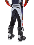 Alpinestars Youth 2024 Racer Hoen Pants, calças de motocross, cinzento claro com detalhes em laranja vibrante e preto, vista traseira com painéis pretos no assento e pernas, marca proeminente na parte traseira da cintura, usadas com botas de motocross pretas e brancas para corridas fora de estrada