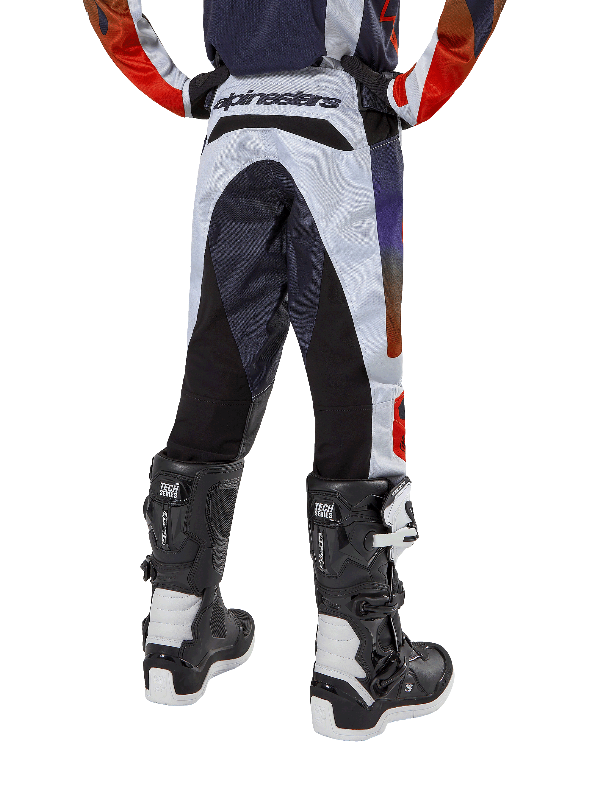 Alpinestars Youth 2024 Racer Hoen Pants, calças de motocross, cinzento claro com detalhes em laranja vibrante e preto, vista traseira com painéis pretos no assento e pernas, marca proeminente na parte traseira da cintura, usadas com botas de motocross pretas e brancas para corridas fora de estrada