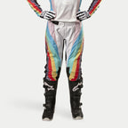 Alpinestars Stella Techstar Pants 2024, calças de motocross para mulher, pretas multicolor com riscas diagonais vibrantes em branco, azul, vermelho e amarelo, usadas com botas e luvas de motocross pretas, design inspirado na competição para performance todo-o-terreno.