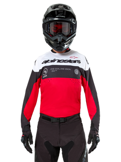 Alpinestars Pro-Dura Jersey, camisola de motocross, preta, vermelho brilhante e branca, usada com capacete e óculos de proteção pretos, design desportivo com logótipo Alpinestars em destaque e perfurações a laser, equipamento de performance para enduro e corridas todo-o-terreno