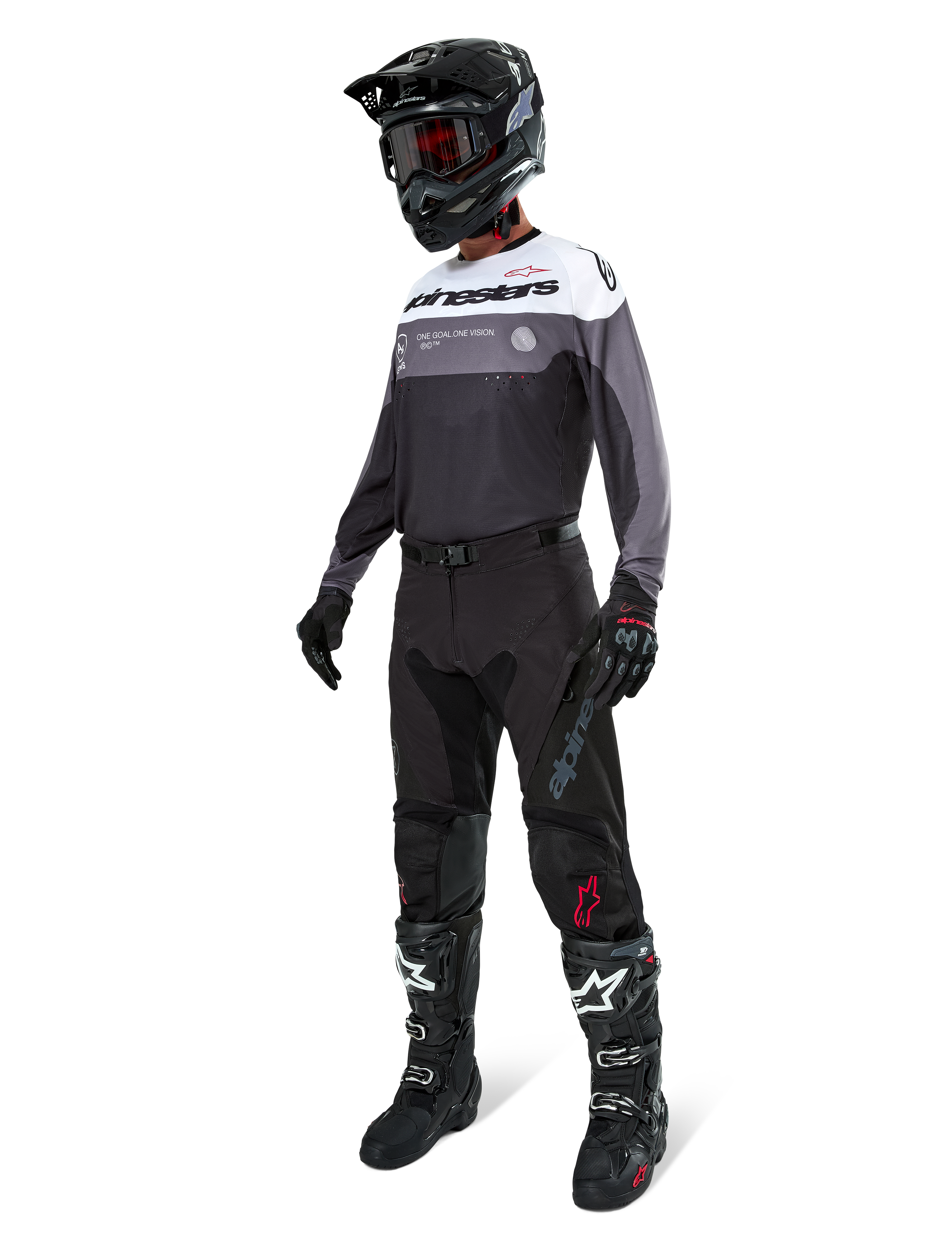 Camisola Alpinestars Pro-Dura em Black Magnet White, vestida por um piloto de motocross com equipamento completo, incluindo calças pretas, capacete preto com óculos e botas pretas e brancas. A camisola apresenta um design técnico de blocos de cor com painéis brancos, cinzentos e pretos, concebida para performance em enduro e todo-o-terreno.