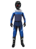 Piloto de motocross com equipamento de corrida completo, camisola Pro-Dura em azul-marinho, azul vivo e branco, calças a condizer em azul e azul-marinho, capacete preto com óculos vermelhos, botas pretas e brancas, conjunto coordenado para enduro e condução off-road