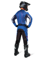 Piloto de motocross visto de costas a usar a camisola Alpinestars Pro-Dura em azul marinho e azul brilhante, calças a condizer em azul e preto, capacete de motocross preto com óculos e botas pretas, exibindo um equipamento de corrida off-road coordenado