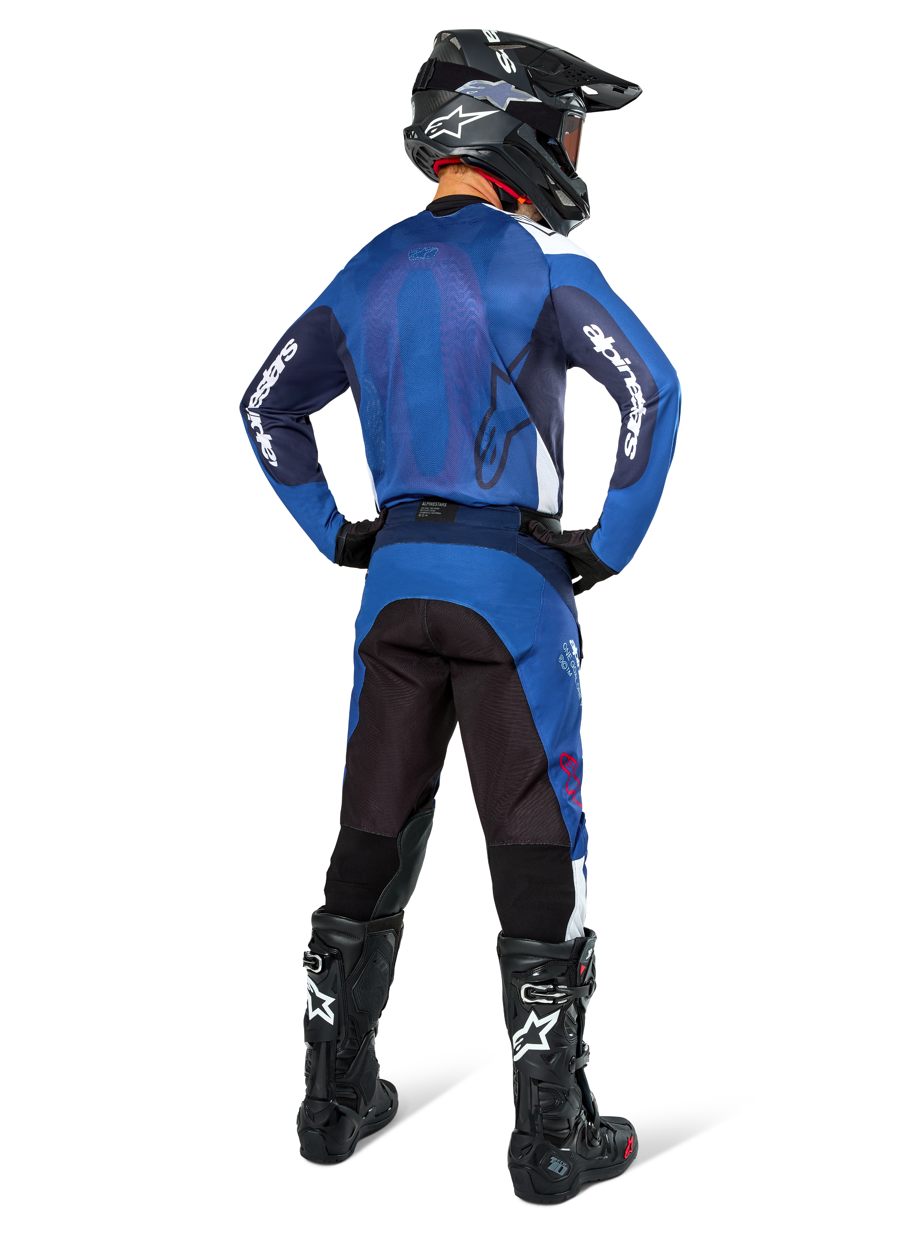 Piloto de motocross visto de costas a usar a camisola Alpinestars Pro-Dura em azul marinho e azul brilhante, calças a condizer em azul e preto, capacete de motocross preto com óculos e botas pretas, exibindo um equipamento de corrida off-road coordenado