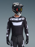 Alpinestars 2026 Racer Air Riway Jersey, camisola de motocross em preto e branco com a marca 'astars', usada por um piloto com capacete, óculos e calças pretas a condizer, com painéis de malha respirável para corridas off-road