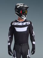 Alpinestars 2026 Racer Air Riway Jersey, camisola de motocross em preto e branco com a marca 'astars', usada por um piloto com capacete, óculos e calças pretas a condizer, com painéis de malha respirável para corridas off-road