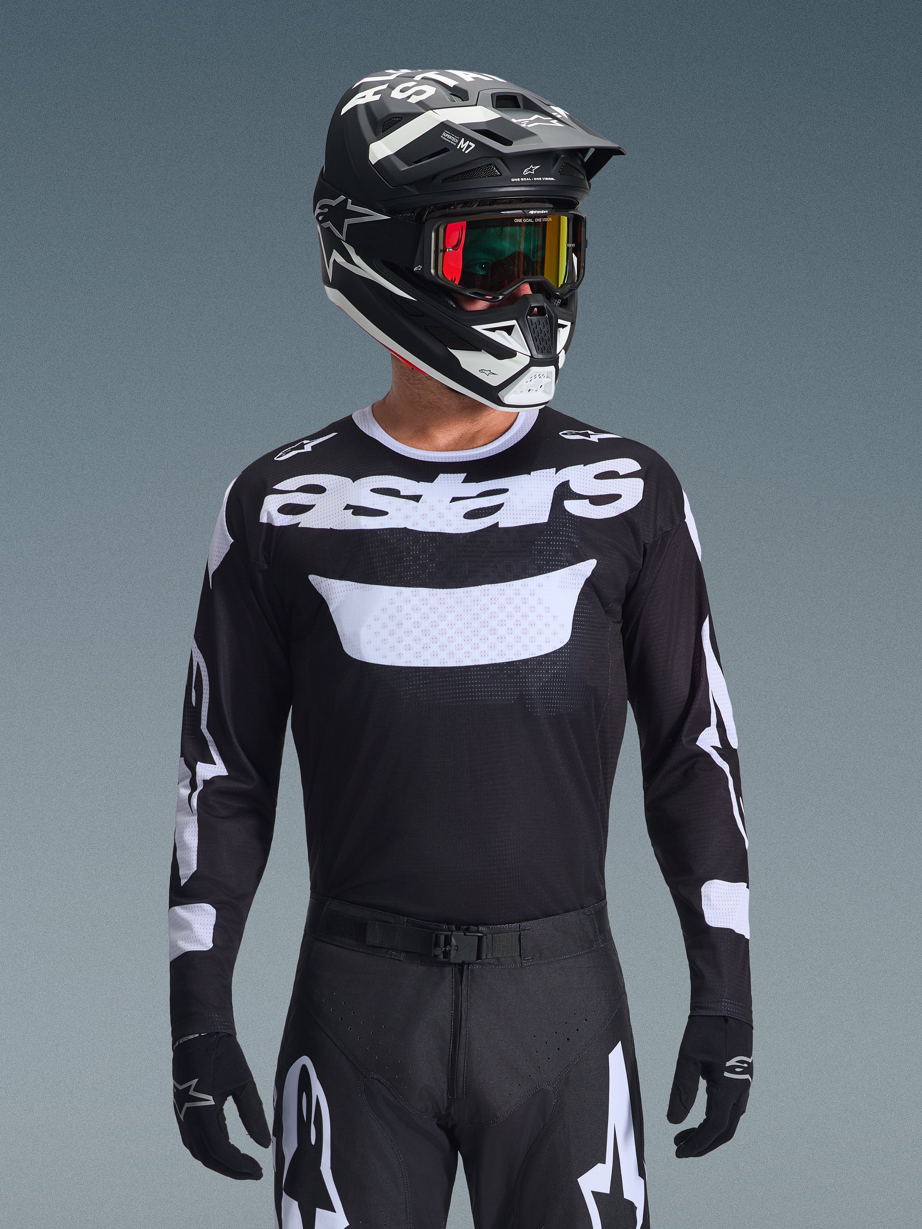 Motocross rider wearing the Alpinestars 2026 Racer Air Riway Gear Set, black jersey with white 'astars' logo and ventilated chest panel, black pants with white accents, matching black and white helmet with iridescent goggles, black gloves, high-performance motocross gear in black and white.