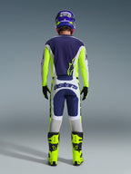 Motocross rider from behind wearing the Alpinestars 2026 Racer Air Riway Gear Set, Blue jersey with fluo yellow and light gray accents, white and blue pants with fluo yellow side panels, fluo yellow boots with black details, matching blue and yellow helmet, professional gear for warm-weather off-road riding