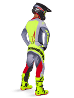 Motocross rider from behind wearing the Alpinestars 2025 Techstar Melt Jersey in Bright Red Gray, featuring a bright yellow back panel and gray sleeves, matching gray and red pants with yellow branding, bright yellow motocross boots, and a black helmet with yellow goggles, coordinated off-road racing kit