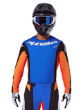 Alpinestars 2025 Techstar Melt Jersey, camisola de motocross azul e laranja com painéis laterais pretos, usada com capacete preto e óculos azuis, com perfurações a laser respiráveis no peito e corte atlético de corrida para performance em todo-o-terreno
