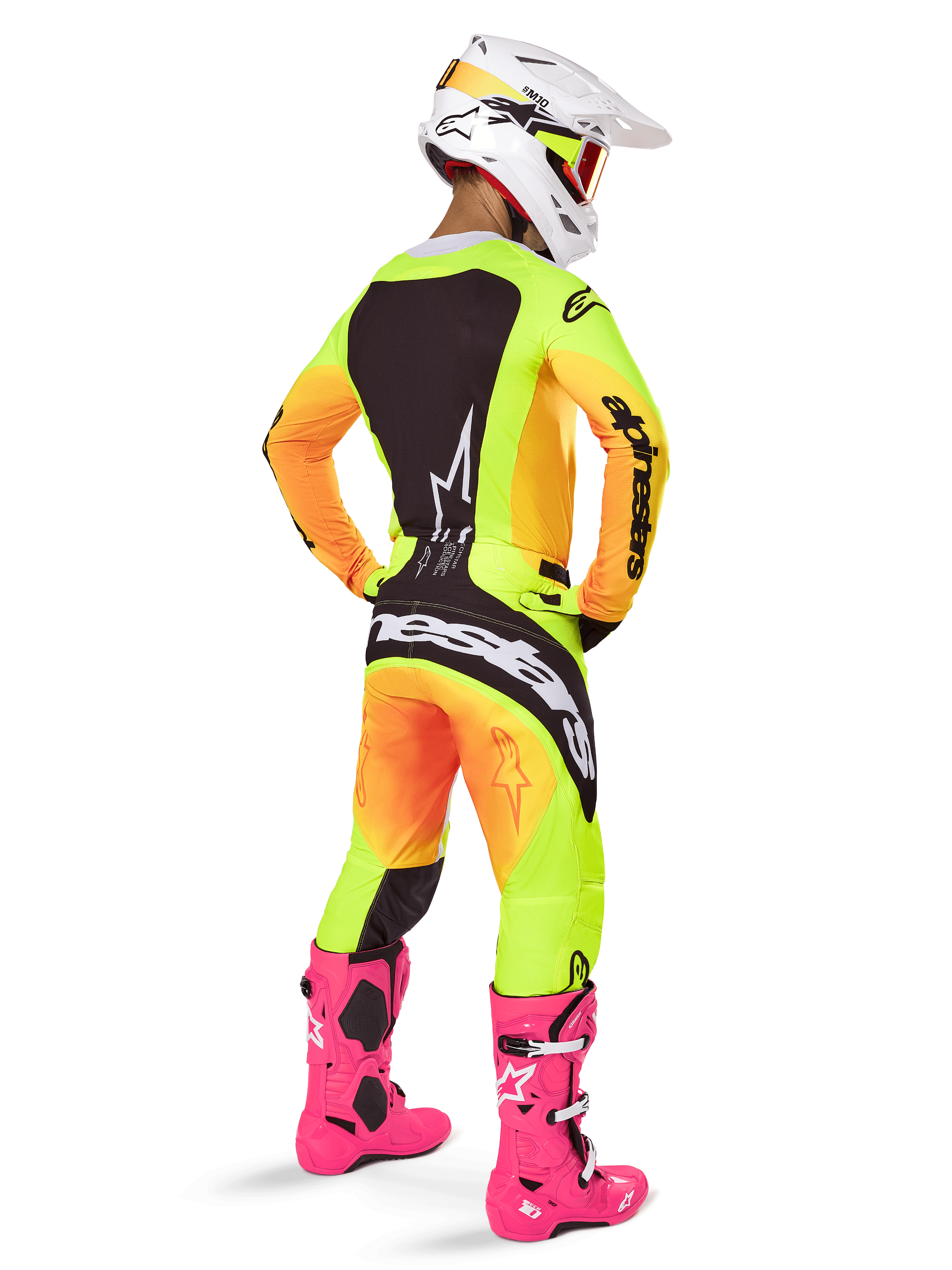 Piloto de motocross visto de costas a usar a camisola Alpinestars 2025 Techstar Melt, com gradiente vibrante de amarelo e laranja e secções pretas, calças de motocross a condizer, botas cor-de-rosa vibrante e capacete branco, corte atlético para competição todo-o-terreno