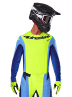Camisola Techstar Melt 2025, camisola de motocross, amarelo fluo e azul, com ventilação cortada a laser e ajuste de corrida, usada por um piloto com capacete preto e luvas amarelo fluo