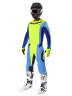 Piloto de motocross a usar a camisola Alpinestars 2025 Techstar Melt, Amarelo Fluo e Azul, combinada com calças a condizer, capacete preto com óculos, luvas amarelas e botas brancas e pretas, equipamento de performance completo para corridas todo-o-terreno