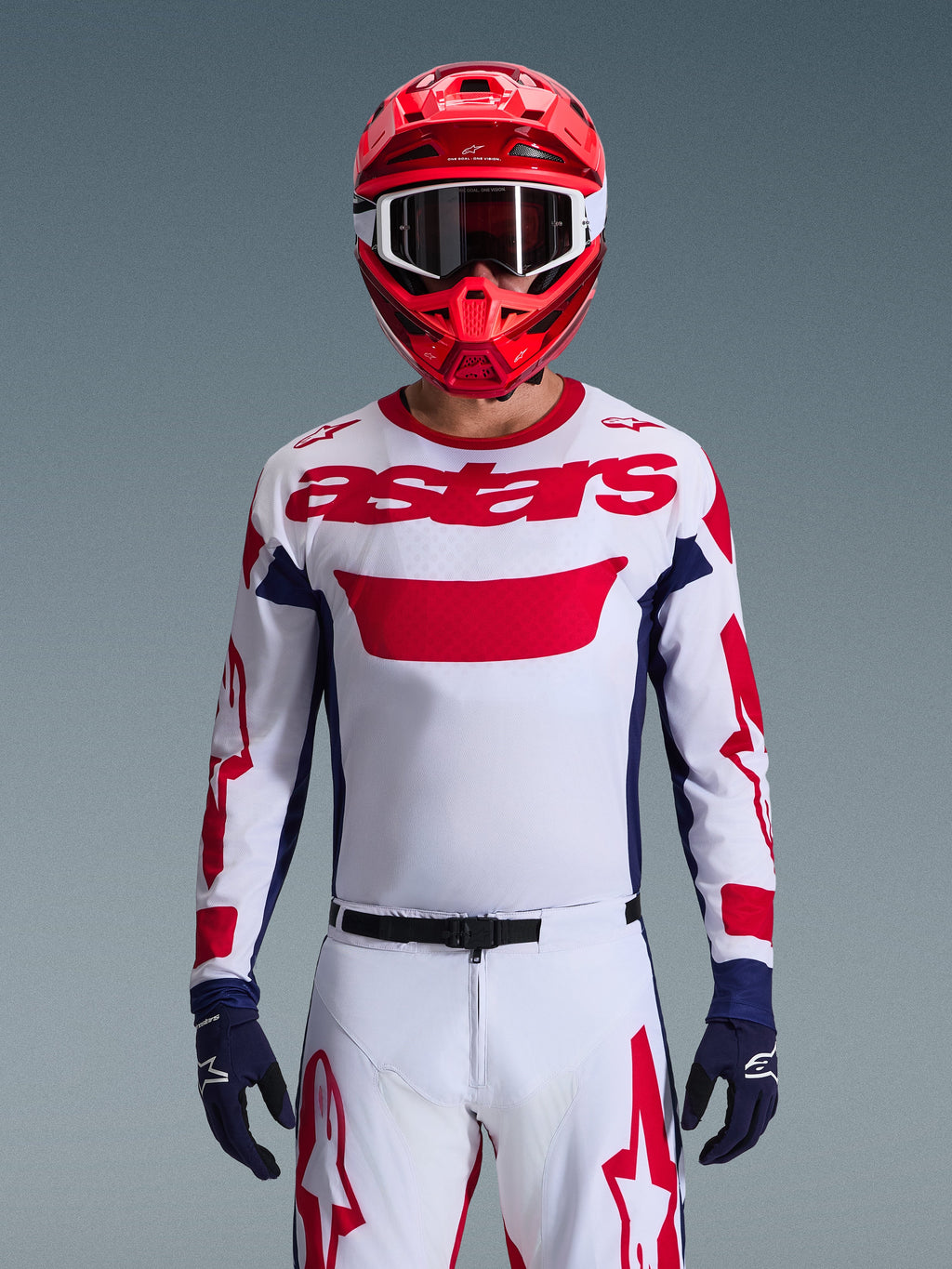 Alpinestars 2026 Racer Riway Gear Set, piloto de motocross com camisola branca, logótipo vermelho e pormenores em azul-escuro, calças brancas com grafismos vermelhos, capacete vermelho com óculos brancos e luvas azul-escuro, equipamento profissional de corrida off-road.