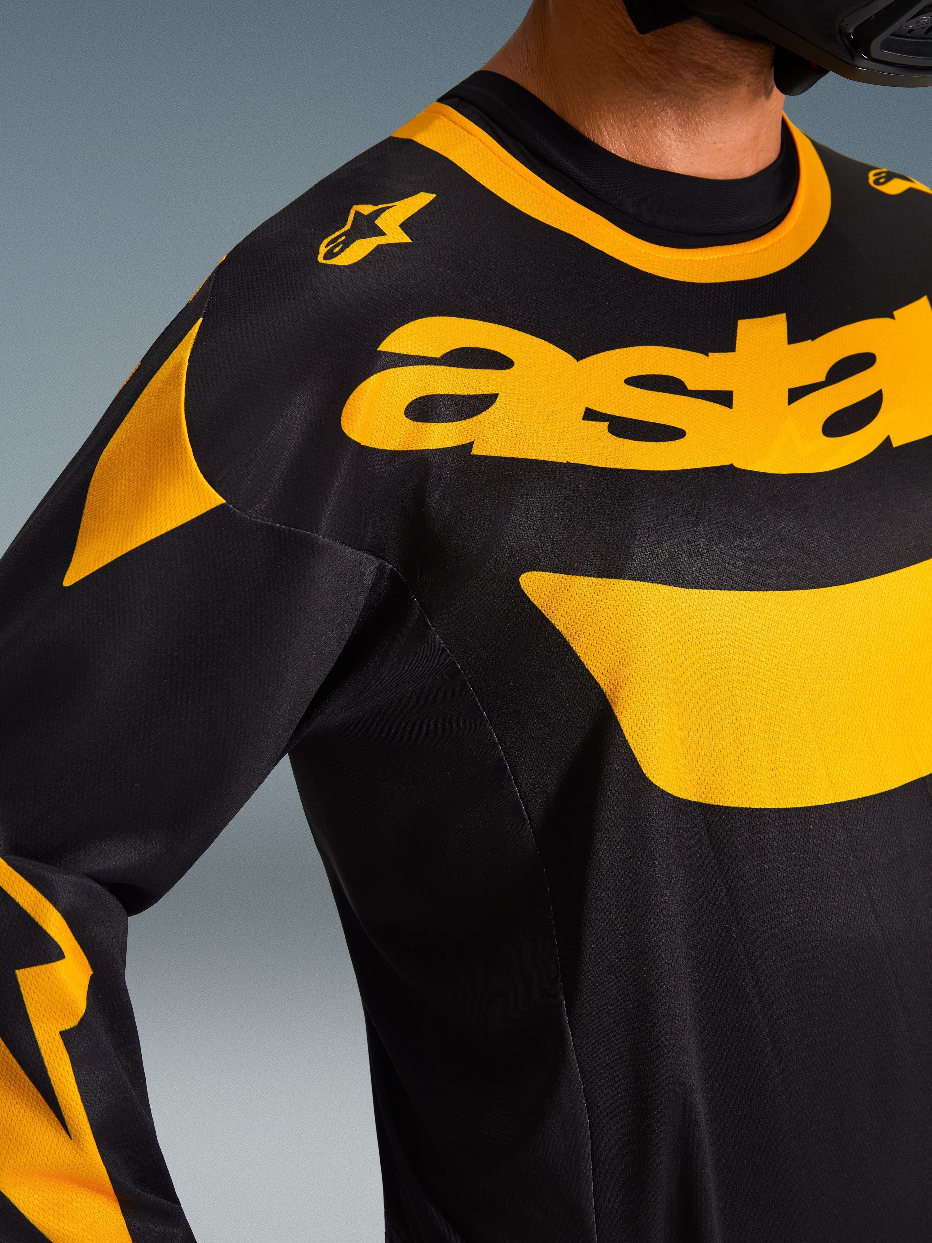 Alpinestars 2026 Racer Riway Jersey, camisola de motocross, amarela e preta, plano aproximado da zona do peito e dos ombros, com a marca 'astars' em amarelo e pormenores gráficos sobre politecido preto, equipamento de performance para todo-o-terreno