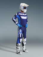 Piloto de motocross com o conjunto de equipamento Alpinestars 2026 Racer Riway em Azul UCLA e Branco, camisola azul e branca com a marca 'astars', calças a condizer, capacete branco com óculos azuis e botas de todo-o-terreno brancas, equipamento de corrida completo para motocross