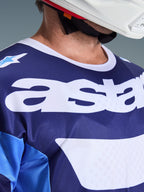 Alpinestars 2026 Racer Riway Jersey, camisola de motocross, azul UCLA e branco, vista de pormenor do peito com logótipo 'astars' de grandes dimensões em branco, gola branca e textura de malha que absorve a humidade, usada com um capacete branco