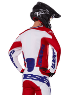 Alpinestars 2025 Racer Veil Jersey and Pants, conjunto de equipamento de motocross, vermelho vivo, branco e azul, vista traseira do piloto a usar o equipamento a condizer e capacete de motocross preto, com a marca Alpinestars em azul em destaque, vestuário técnico de corrida para todo-o-terreno
