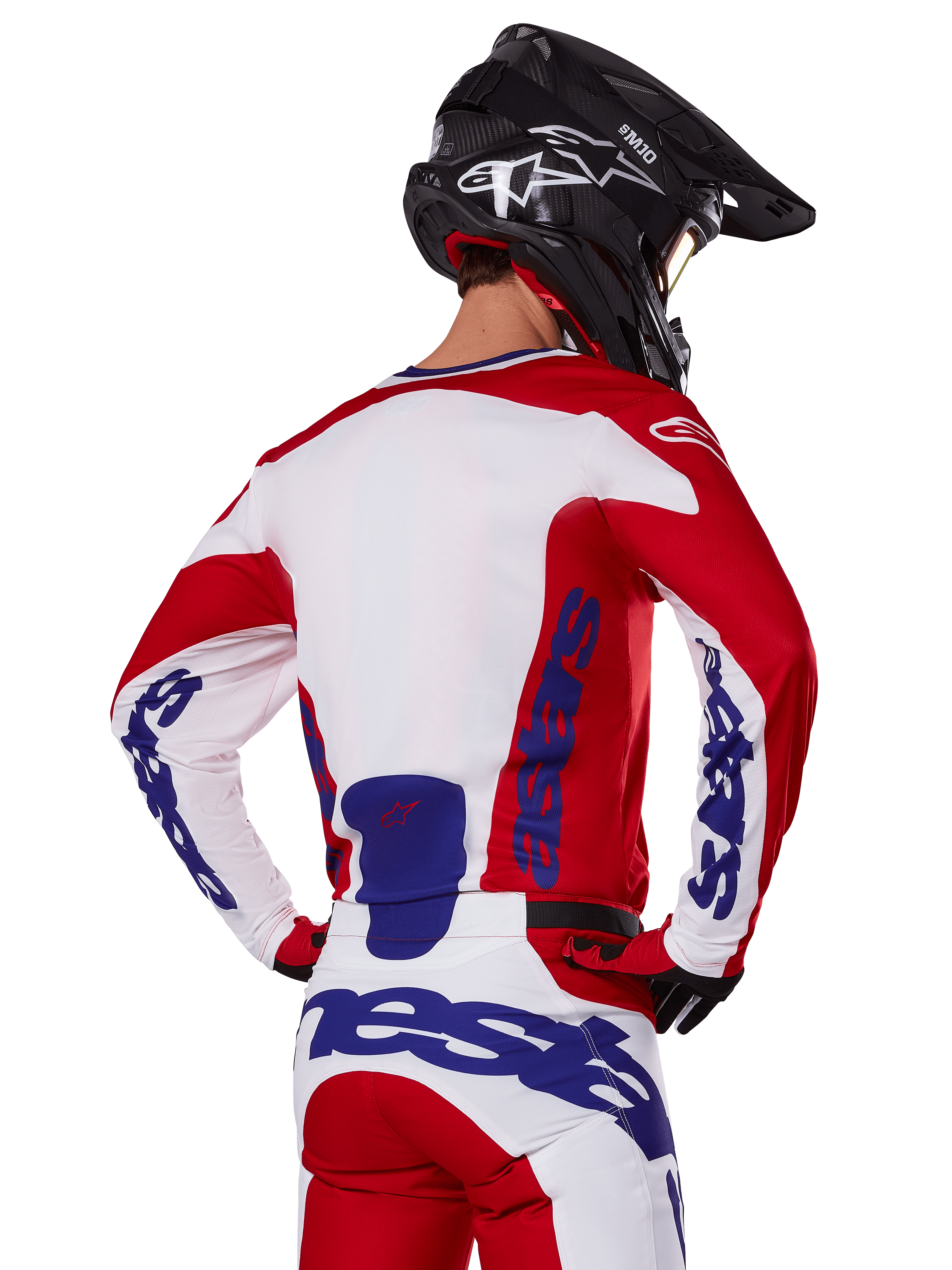 Alpinestars 2025 Racer Veil Jersey and Pants, conjunto de equipamento de motocross, vermelho vivo, branco e azul, vista traseira do piloto a usar o equipamento a condizer e capacete de motocross preto, com a marca Alpinestars em azul em destaque, vestuário técnico de corrida para todo-o-terreno