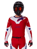 Alpinestars 2025 Racer Veil Jersey, camisola de motocross de manga comprida, vermelha, branca e azul, usada com capacete preto e óculos laranja, luvas e calças vermelhas coordenadas, design de alta performance para todo-o-terreno