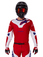 Alpinestars 2025 Racer Veil Jersey, camisola de motocross de manga comprida, vermelha, branca e azul, usada com capacete preto e óculos laranja, luvas e calças vermelhas coordenadas, design de alta performance para todo-o-terreno