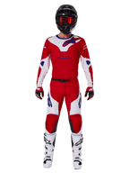 Piloto de motocross com o conjunto de equipamento Alpinestars 2025 Racer Veil, camisola e calças em vermelho vivo e branco com detalhes em azul, capacete preto com óculos vermelhos, botas brancas e luvas vermelhas e pretas, conjunto coordenado para corridas todo-o-terreno