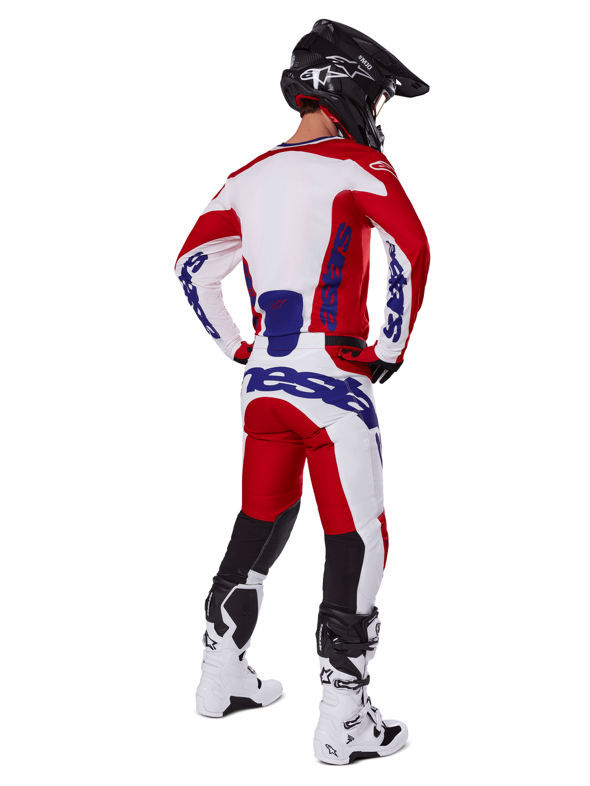 Piloto de motocross visto de costas a usar a camisola e calças Alpinestars 2025 Racer Veil em vermelho e branco, com logótipos azuis, capacete preto e botas brancas, conjunto de equipamento completo para corridas todo-o-terreno